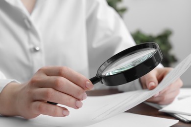 Photo of Woman looking at document through magnifier at table indoors, closeup. Searching concept