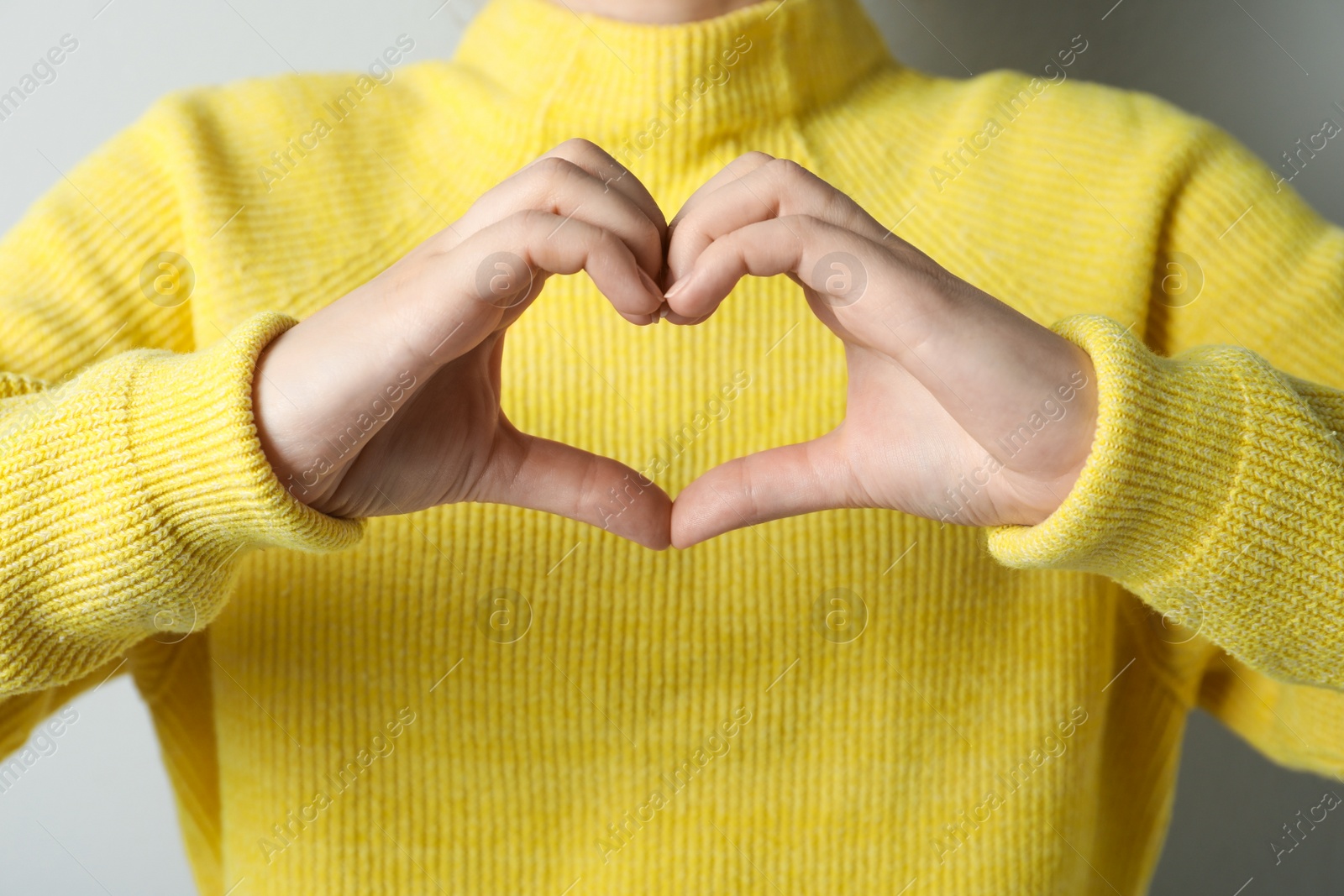 Photo of Woman making heart with her hands on light grey background, closeup