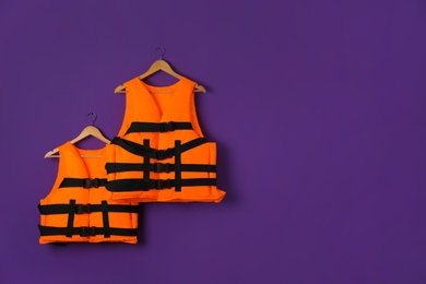 Photo of Orange life jackets on violet background. Space for text