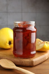 Photo of Tasty homemade quince jam in jar and fruits on wooden table
