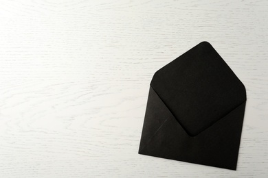 Photo of Black paper envelope on white wooden background, top view. Space for text