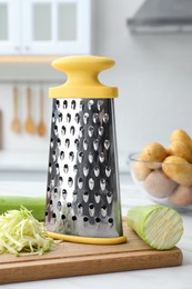 Grater and fresh zucchini on white table in kitchen