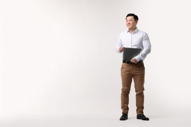 Full length portrait of happy man with laptop on light background. Space for text