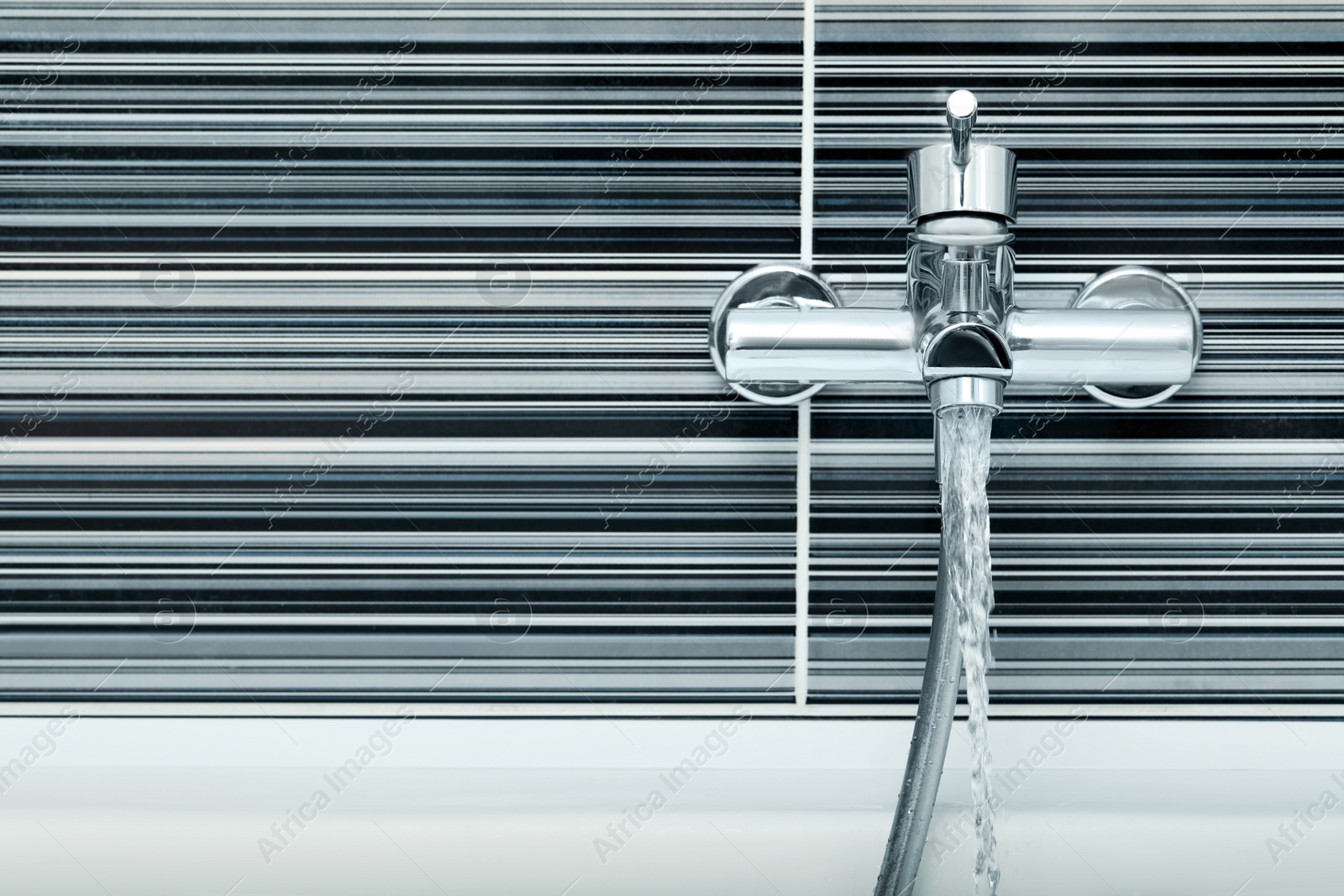 Photo of Water flowing from bath tap installed on black and white wall