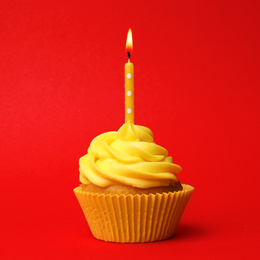 Photo of Delicious birthday cupcake with yellow cream and burning candle on red background