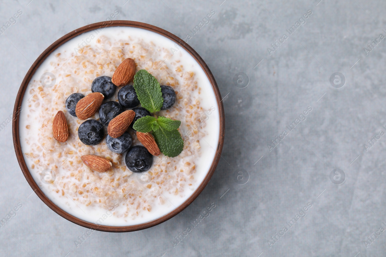 Photo of Tasty wheat porridge with milk, blueberries and almonds in bowl on gray table, top view. Space for text