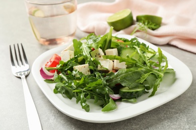 Photo of Delicious salad with feta cheese, arugula and vegetables on grey table, closeup