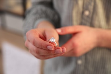 Photo of Woman holding wedding ring indoors, closeup. Divorce concept