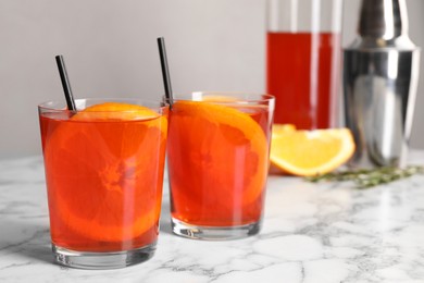 Aperol spritz cocktail, orange slices and straws in glasses on white marble table