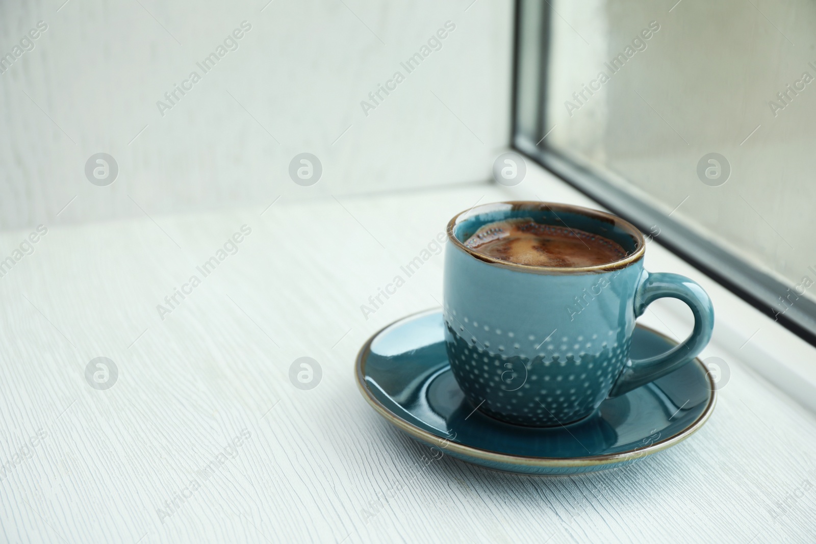 Photo of Cup of hot aromatic coffee on white wooden windowsill, space for text. Rainy weather