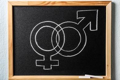 Small blackboard with drawn gender symbols on white wall. Sex education