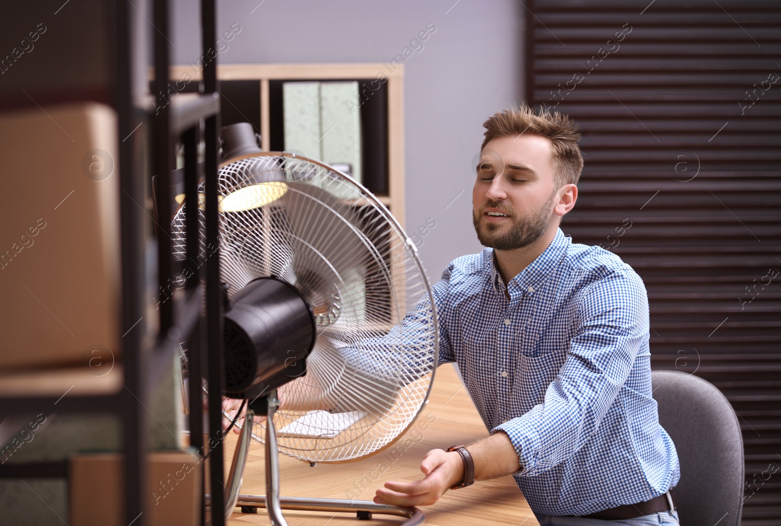 Photo of Man enjoying air flow from fan at workplace