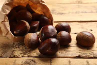 Photo of Sweet fresh edible chestnuts in paper bag on wooden table, closeup