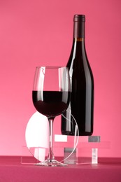 Stylish presentation of delicious red wine in bottle and glass on pink background