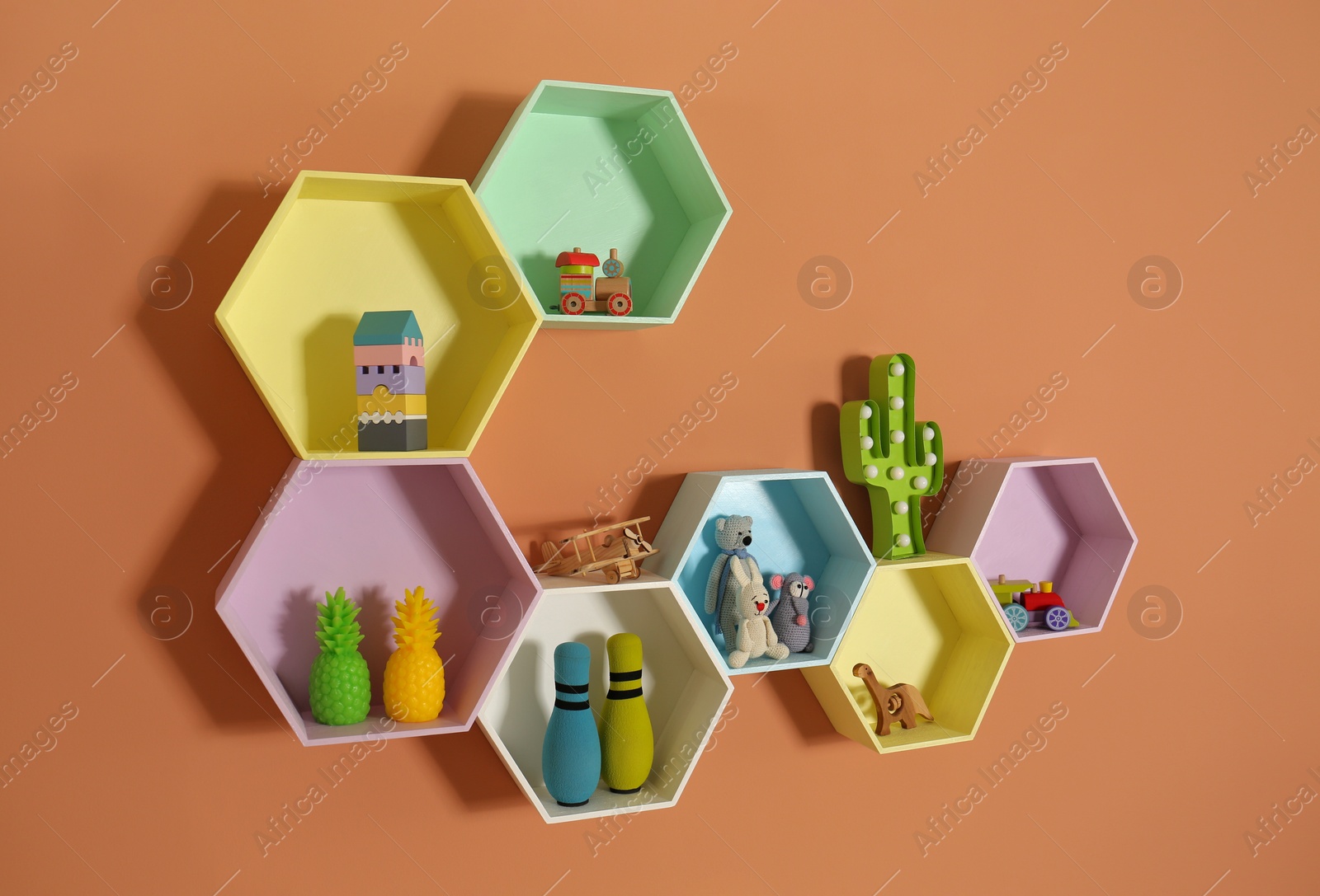 Photo of Hexagon shaped shelves with toys on orange wall. Interior design