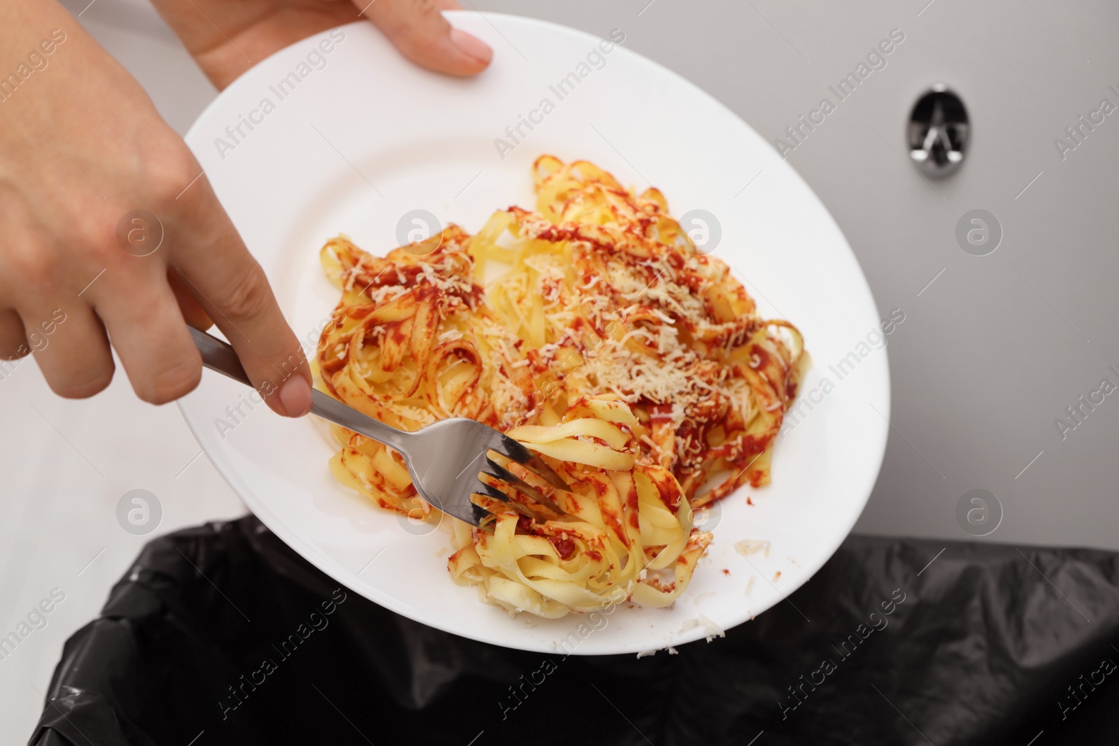 Photo of Woman throwing pasta into bin indoors, closeup