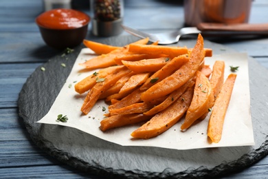 Photo of Slate plate with tasty sweet potato fries on wooden table