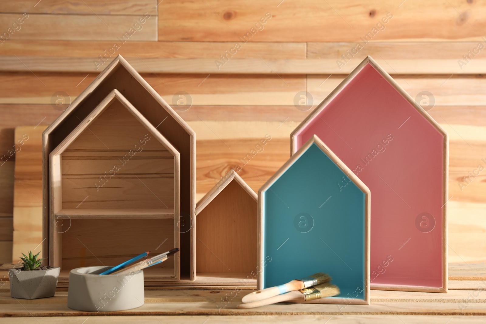 Photo of Painted house shaped shelves, brushes and plant on wooden table. Interior elements