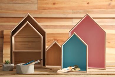 Photo of Painted house shaped shelves, brushes and plant on wooden table. Interior elements