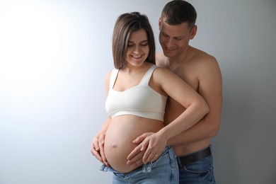 Photo of Man touching his pregnant wife's belly on light background