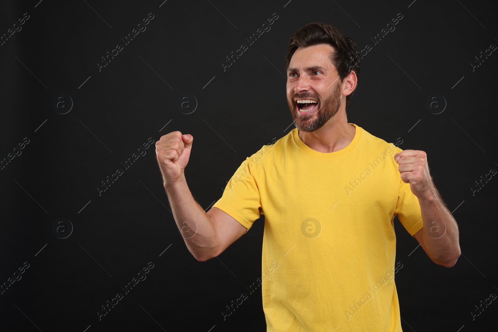 Photo of Emotional sports fan celebrating on black background, space for text