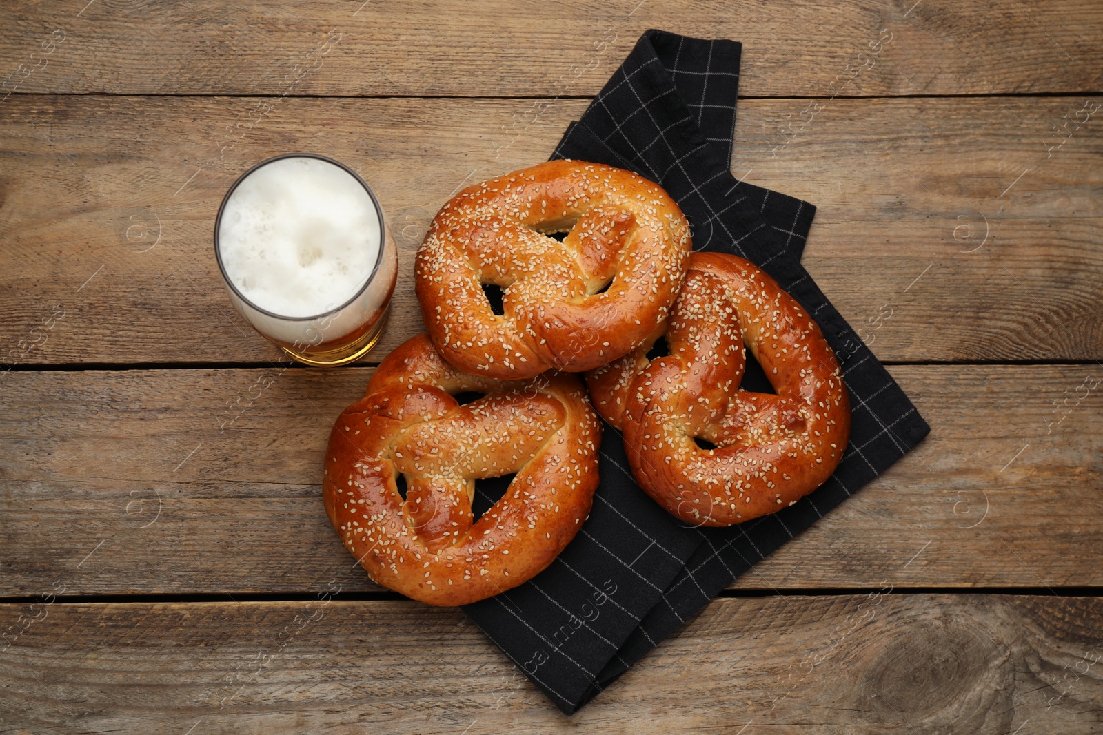 Photo of Tasty pretzels and glass of beer on wooden table, flat lay