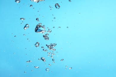 Photo of Air bubbles in water on light blue background. Space for text