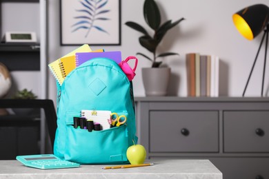 Photo of Turquoise backpack and different school stationery on table indoors, space for text