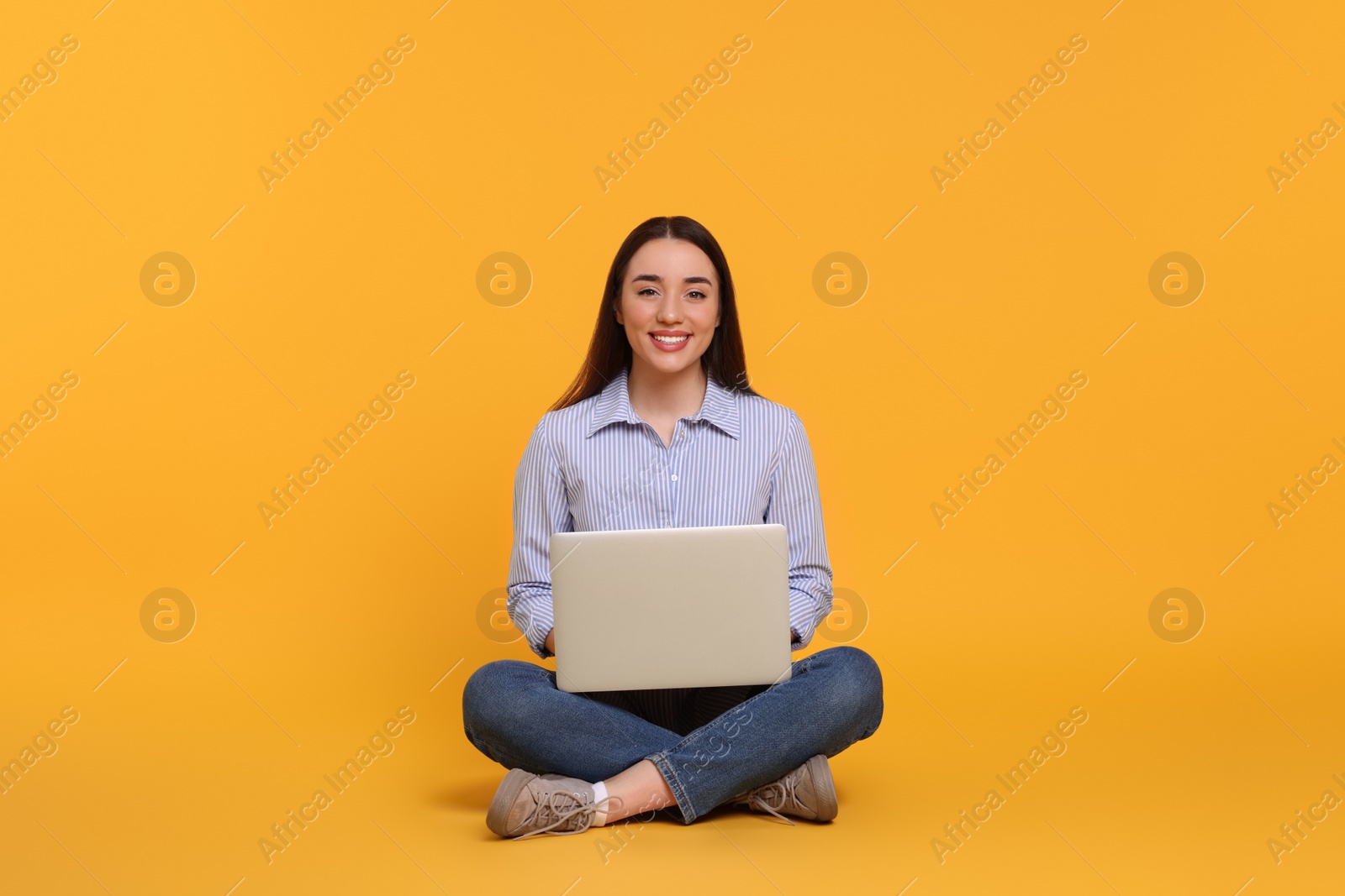 Photo of Smiling young woman working with laptop on yellow background
