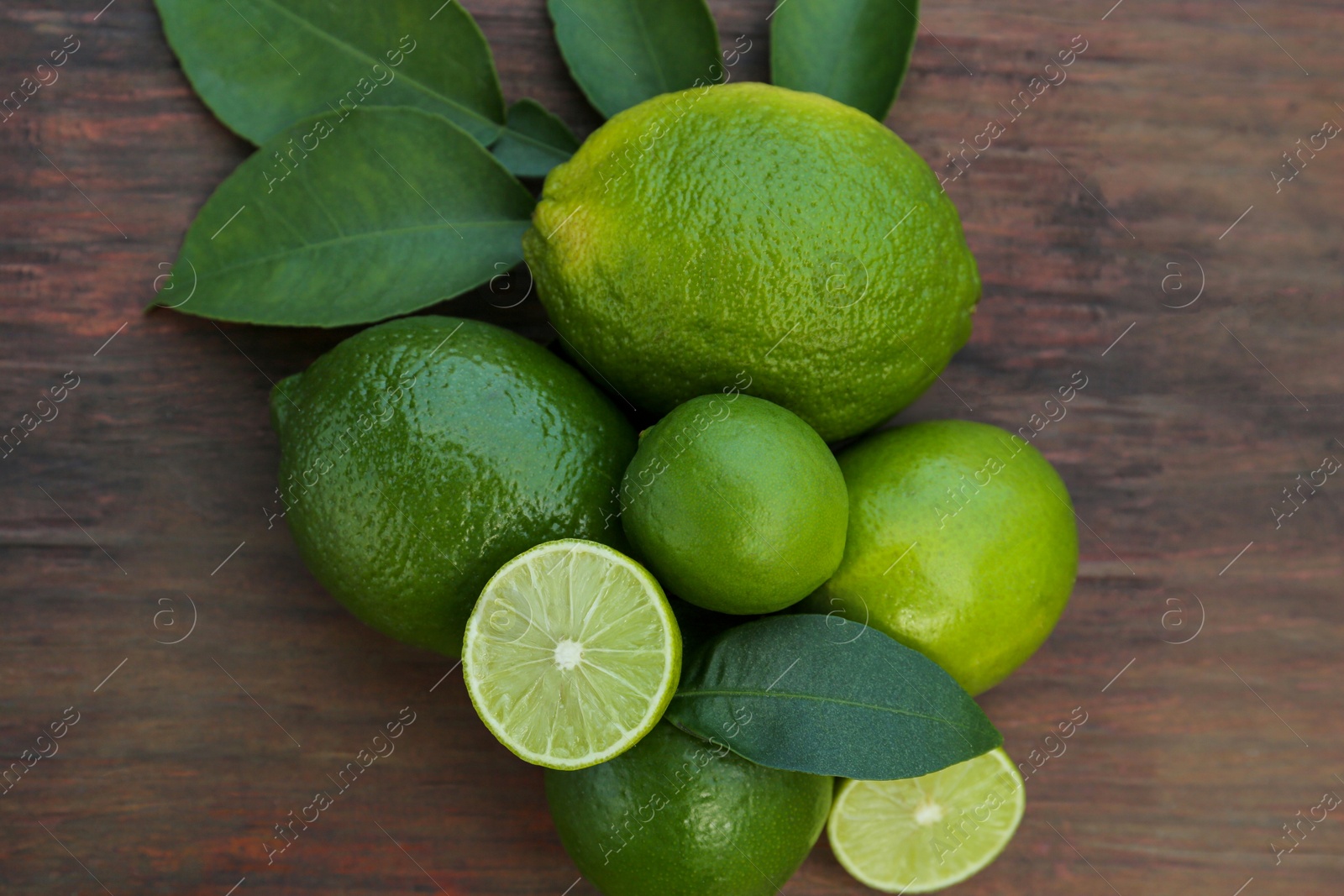 Photo of Whole and cut fresh ripe limes with green leaf on wooden table, flat lay