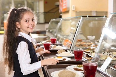 Cute girl near serving line with healthy food in school canteen