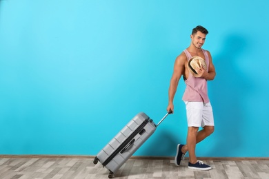 Photo of Young man walking with suitcase on color wall background. Space for text