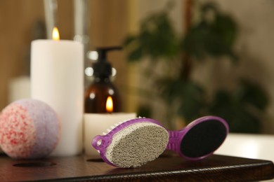 Pedicure tool with pumice stone and foot file near burning candles on wooden caddy in bathroom