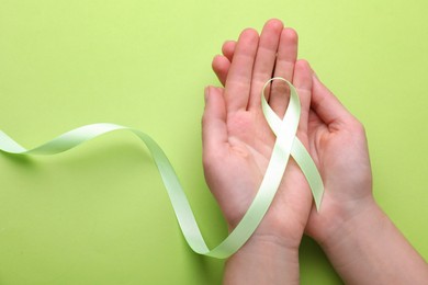 World Mental Health Day. Woman holding green ribbon on color background, top view with space for text