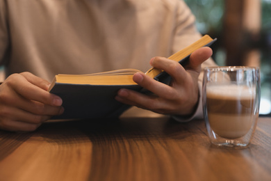 Photo of Man with coffee reading book at wooden table, closeup