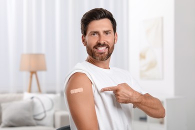Photo of Man pointing at sticking plaster after vaccination on his arm at home
