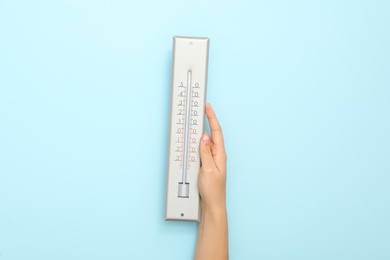 Photo of Woman with weather thermometer on light blue background, closeup