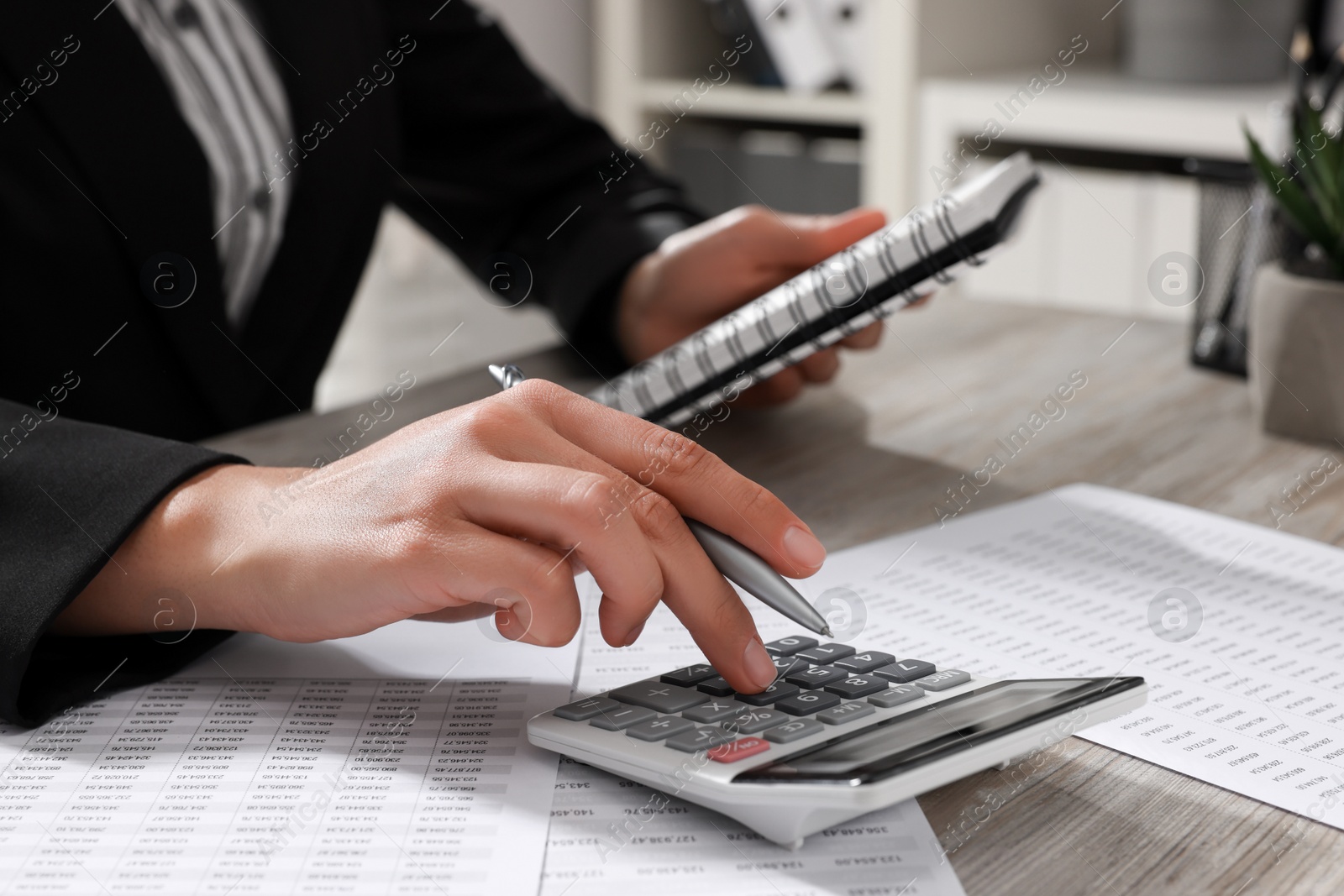 Photo of Woman using calculator at light wooden table in office, closeup