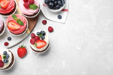 Sweet cupcakes with fresh berries on light marble table, flat lay. Space for text