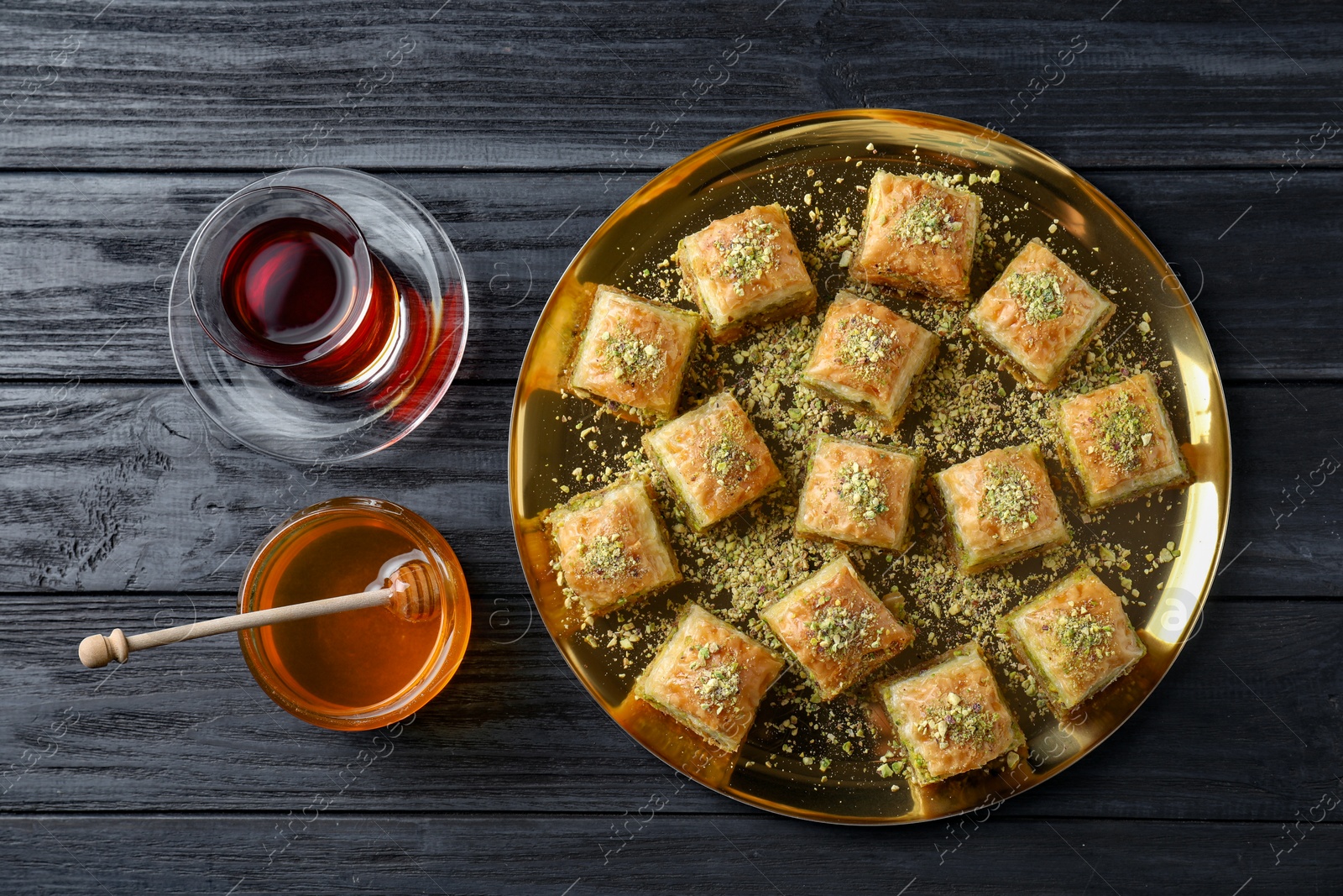 Photo of Delicious fresh baklava with chopped nuts served on black wooden table, flat lay. Eastern sweets