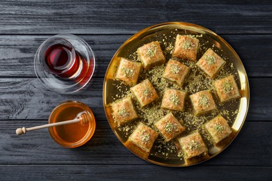 Photo of Delicious fresh baklava with chopped nuts served on black wooden table, flat lay. Eastern sweets