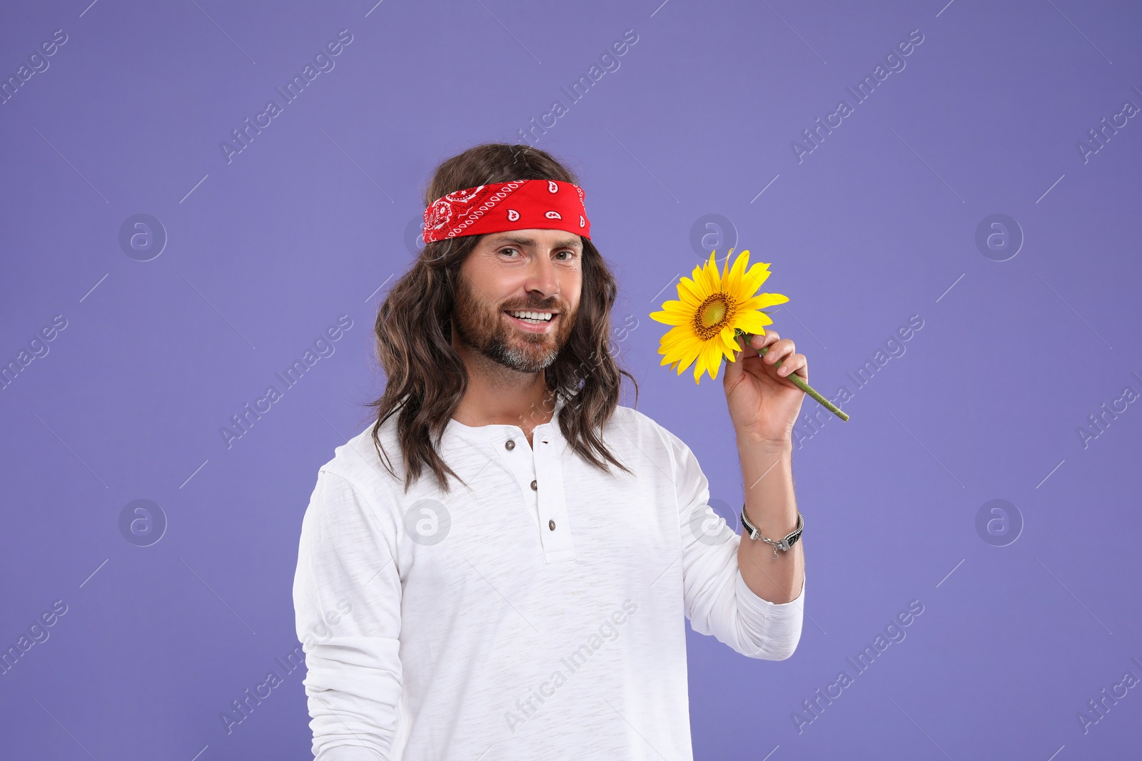 Photo of Stylish hippie man with sunflower on violet background