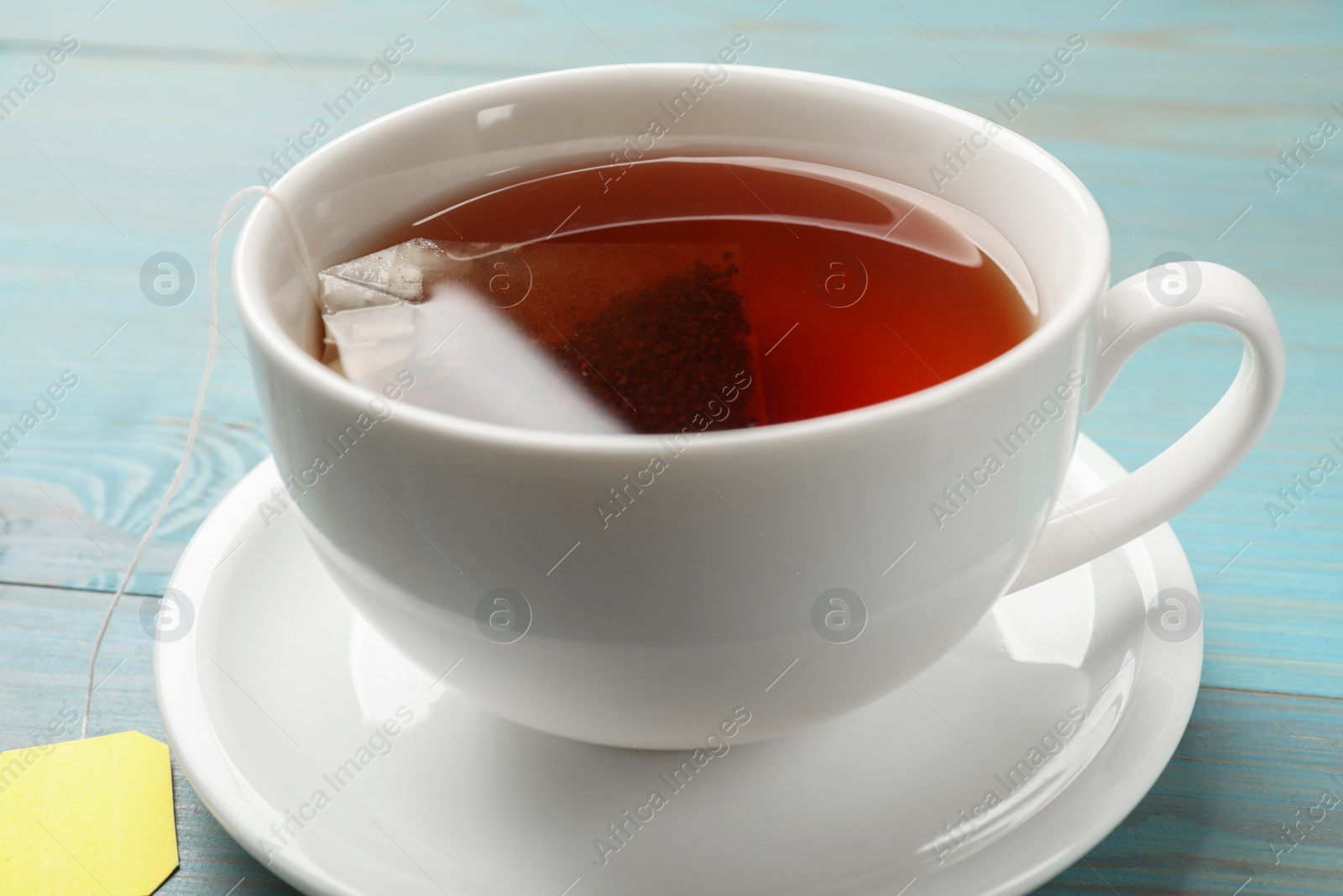 Photo of Tea bag in cup with hot drink on light blue wooden table, closeup