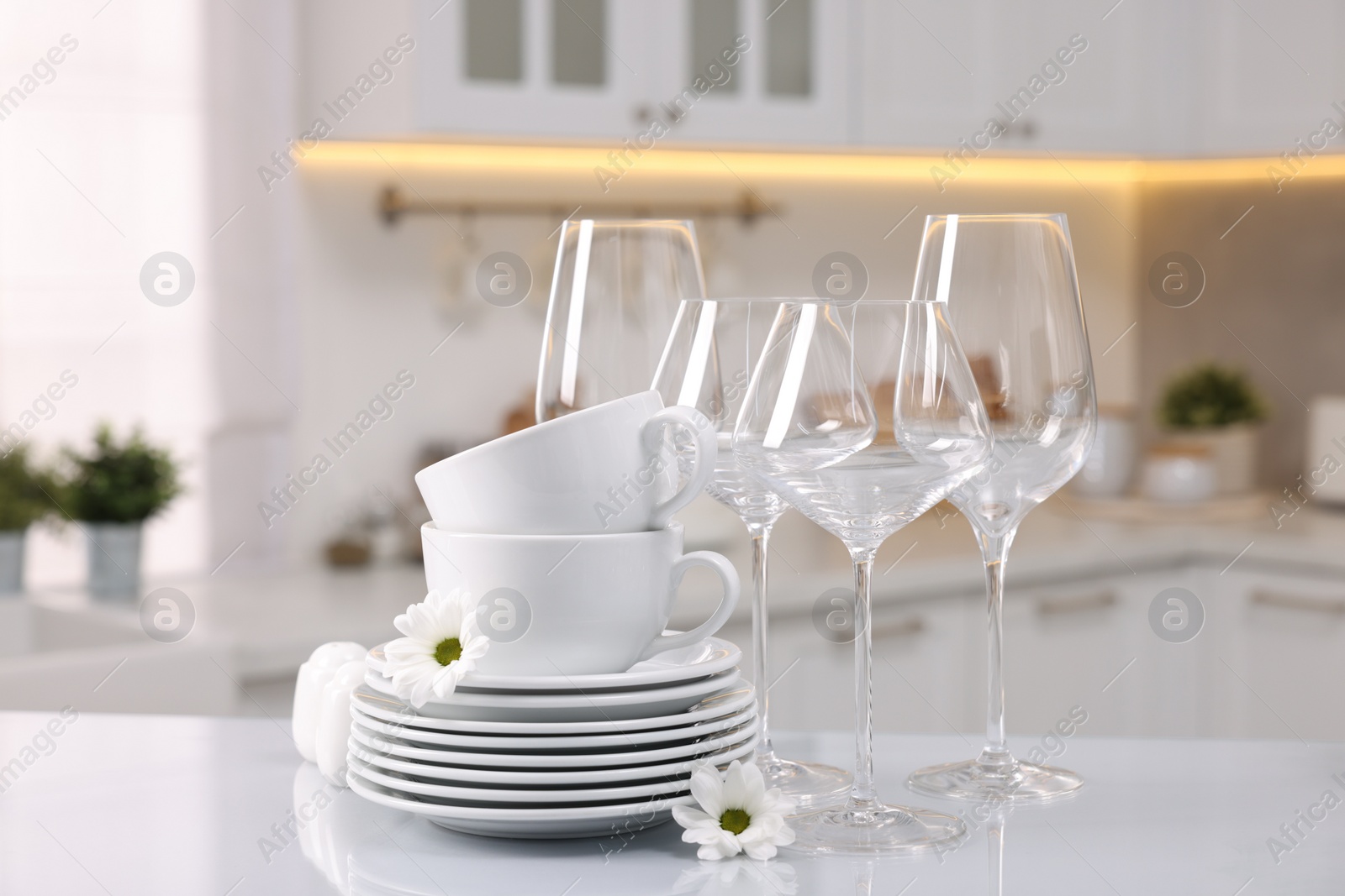 Photo of Set of clean dishware, glasses and flowers on table in kitchen