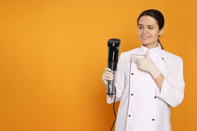 Chef pointing on sous vide cooker against orange background. Space for text