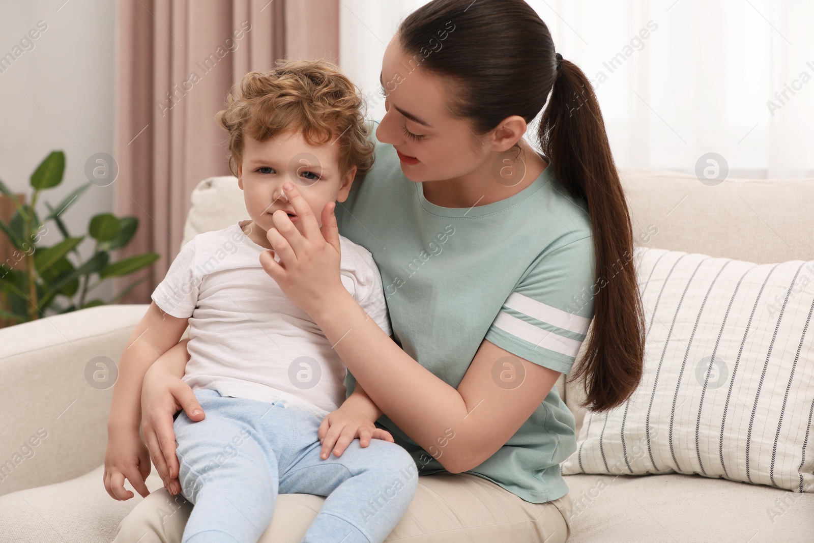 Photo of Mother applying ointment onto her son`s nose on sofa at home