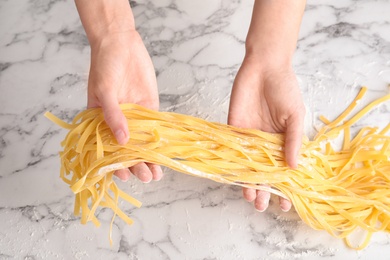 Photo of Woman holding raw egg noodles over marble table, closeup