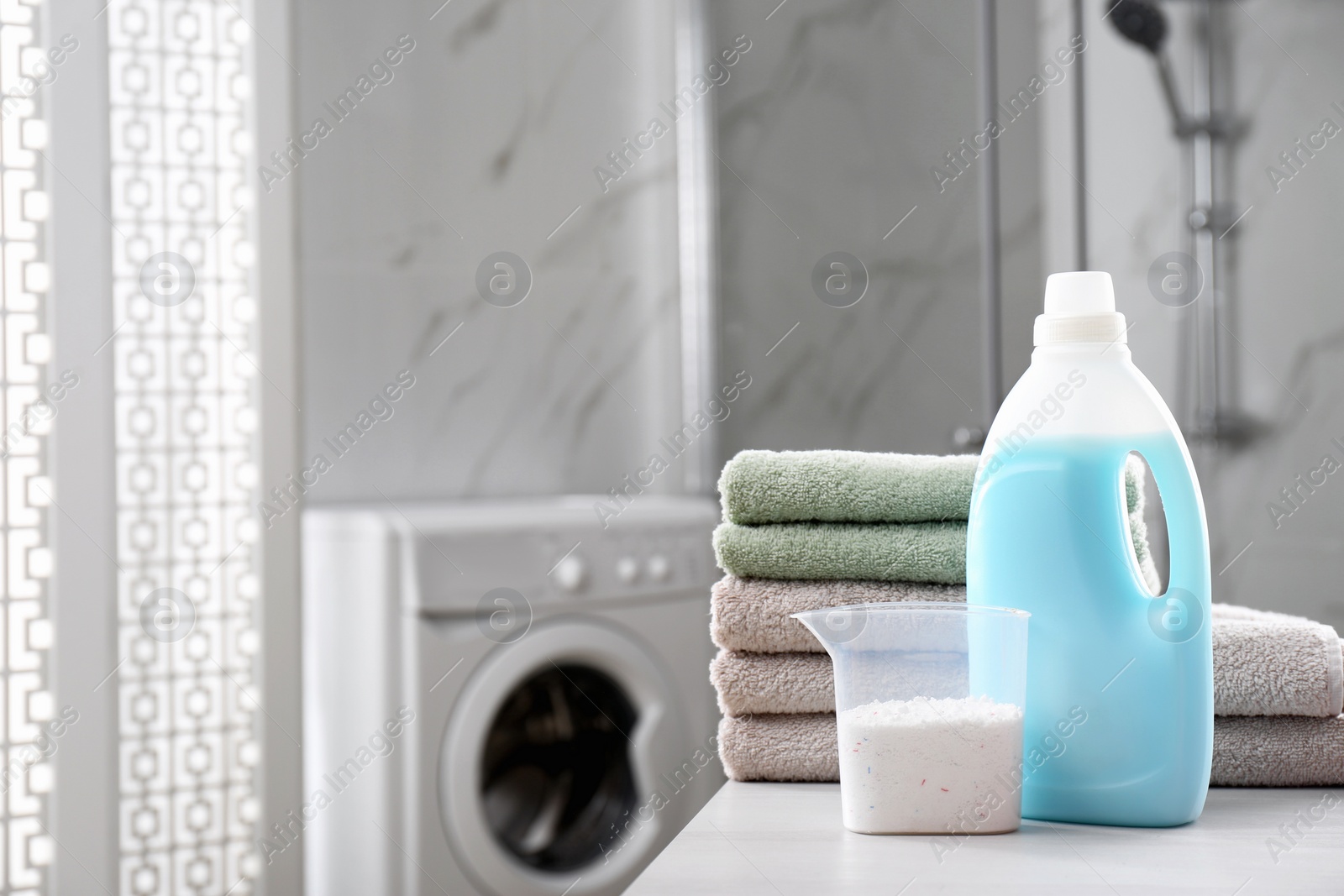 Photo of Stack of folded towels and detergents on white table in bathroom, space for text