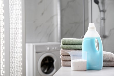 Stack of folded towels and detergents on white table in bathroom, space for text