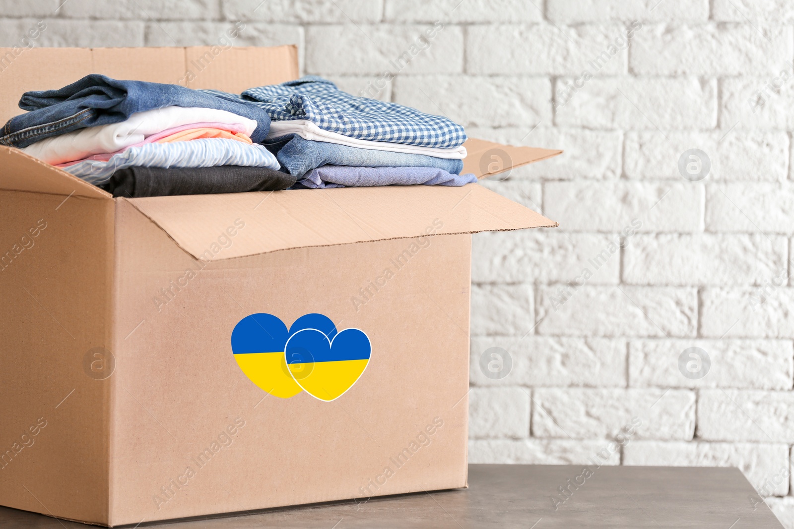 Image of Humanitarian aid for Ukrainian refugees. Donation box with clothes on table near brick wall